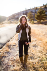 Senior girl wearing brown and white leather bomber jacket from Still In Style Boutique walking next to road in Rogers Canyon