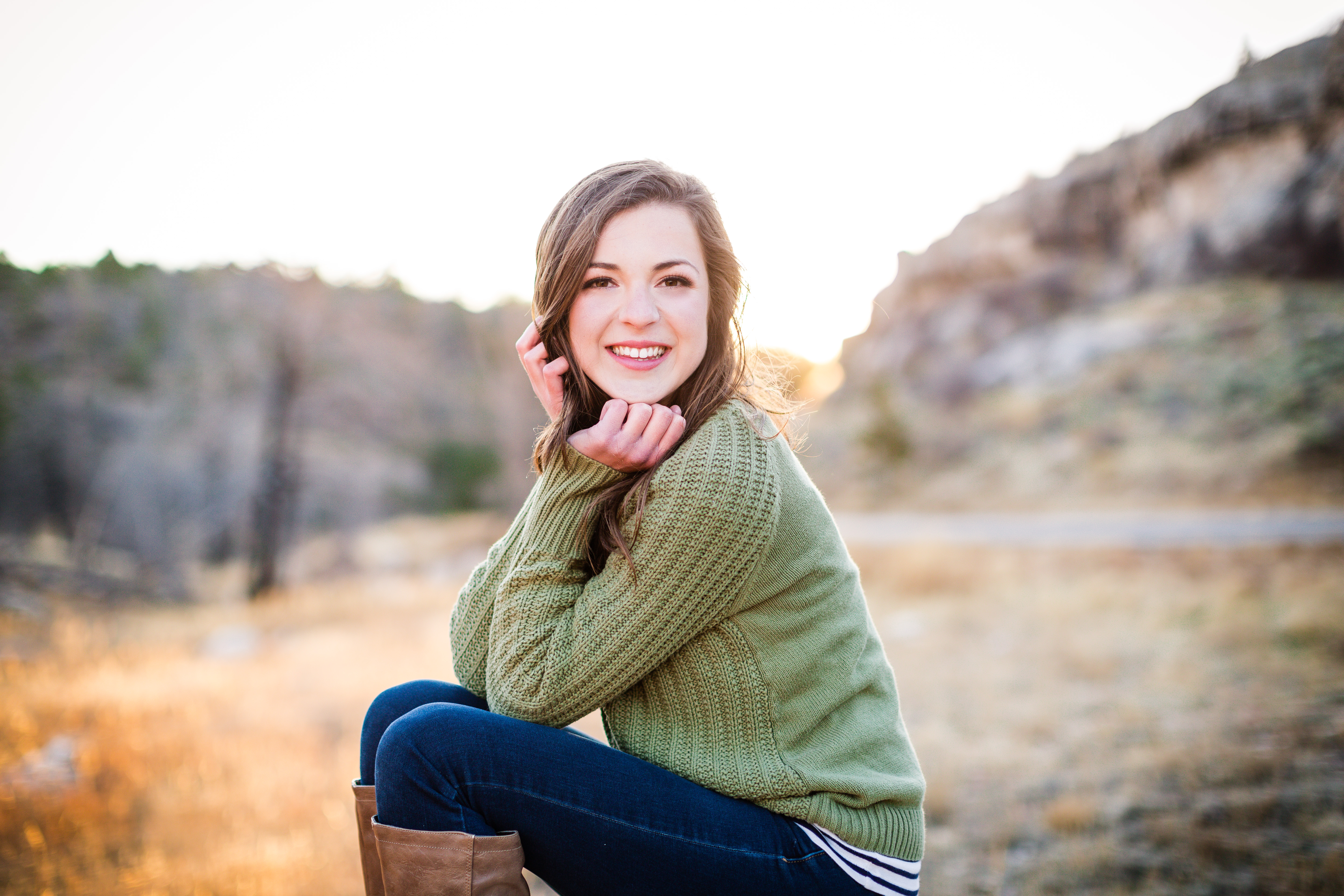 senior girl wearing a sage green sweater sitting with right arm resting across knees and chin resting in both of her hands