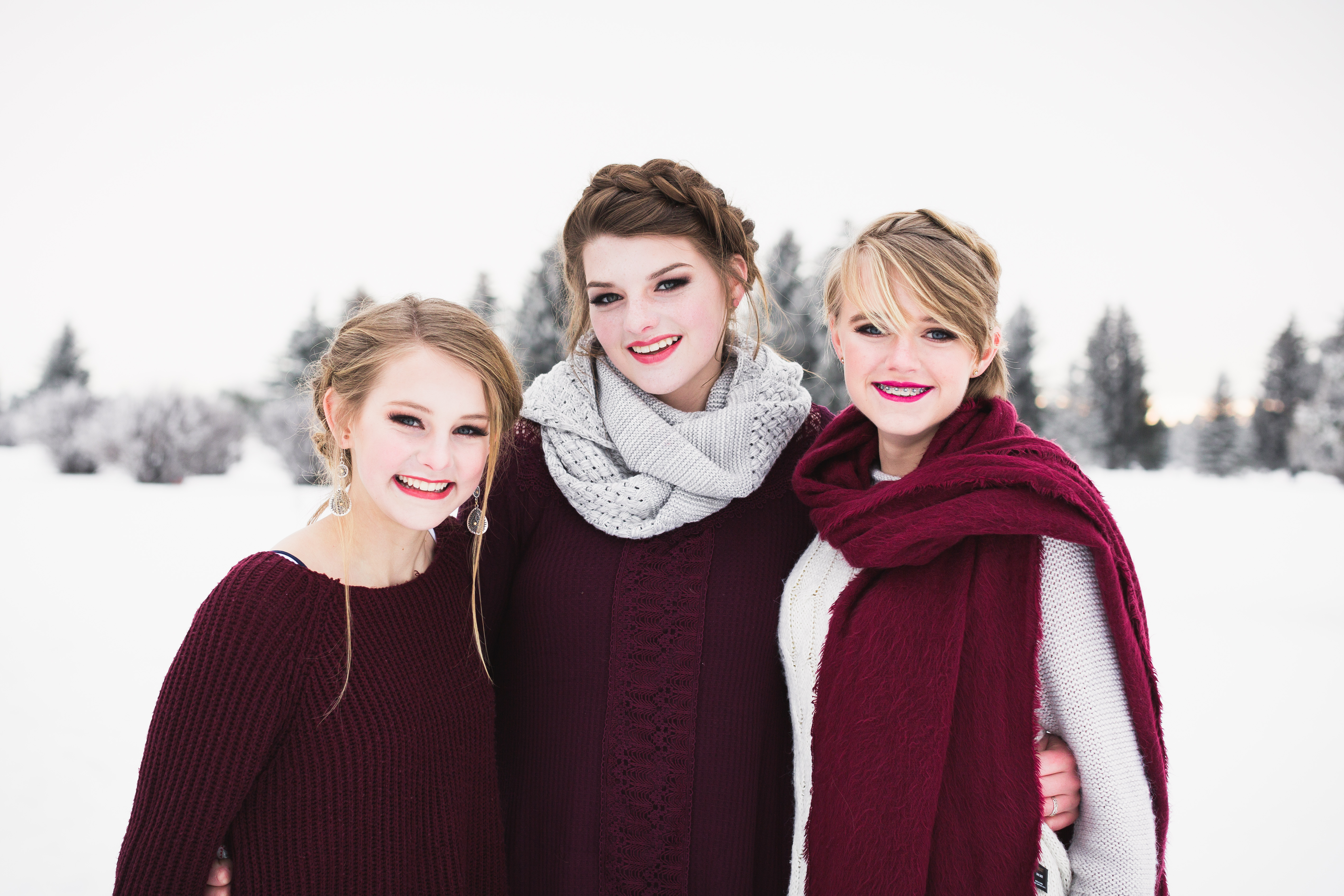 close up of two blonde and one brunette senior girls wearing maroon and white outfits smiling and standing in snow