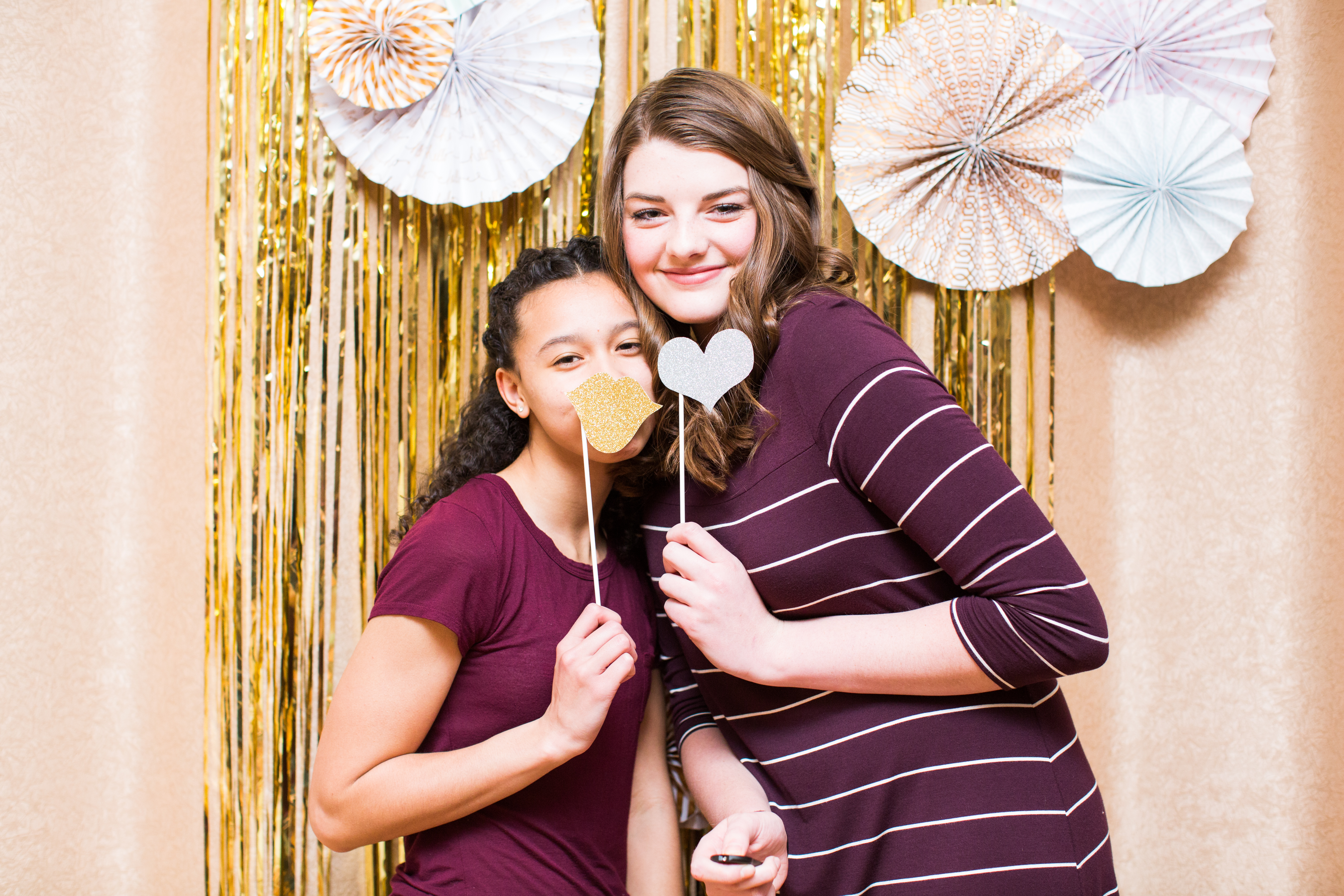 two girls smiling holding gold and silver props in photo booth at Little Birds photography's Glitter & Glam Night
