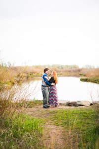 couple is standing facing each other holding hands on a river bank.