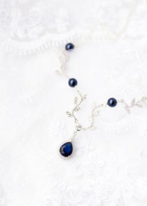 An intricate navy blue and sliver necklace laying on top of the bride's lace veil