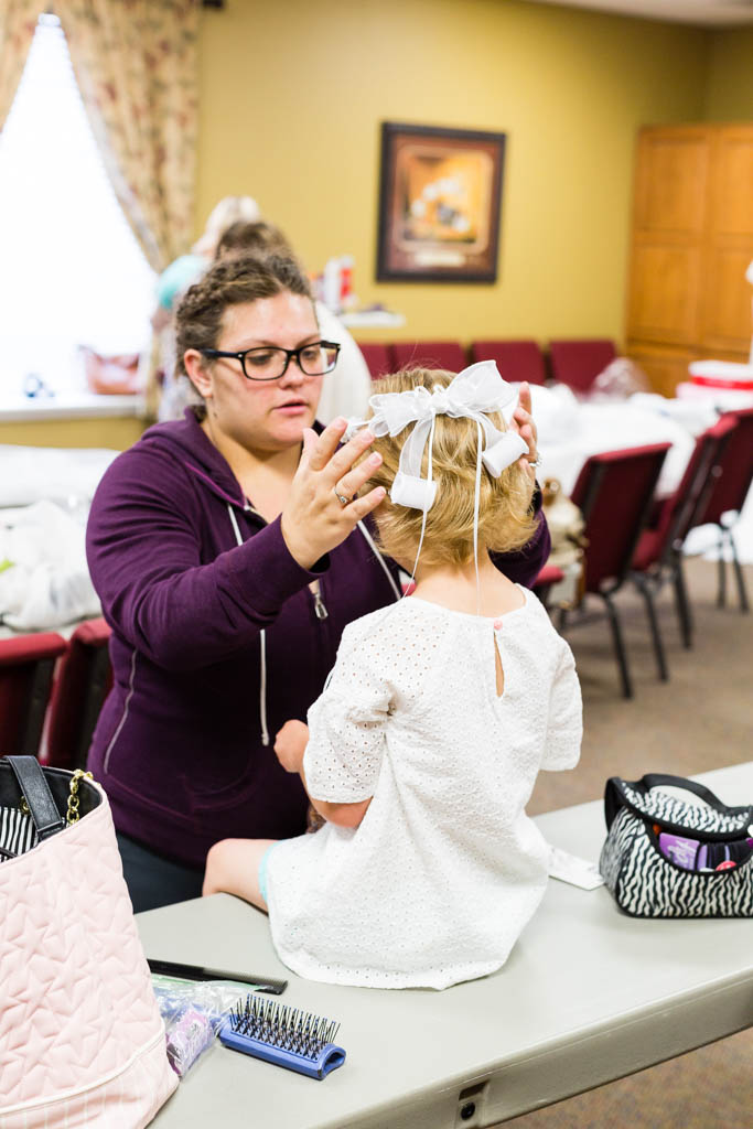 woman places headband on the flower girl's short blonde he=air while they get ready