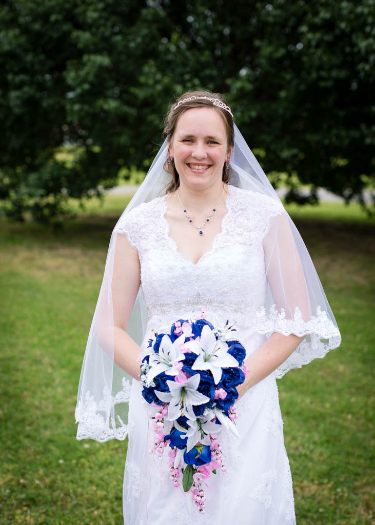 bride wearing a lace dress and matching veil holds her bouquet and smiles