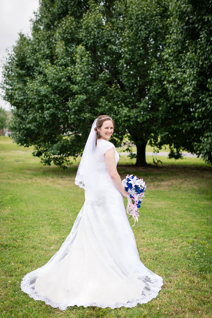 bride wearing a lace dress with short sleeves and a chapel train looks over her shoulder and smiles