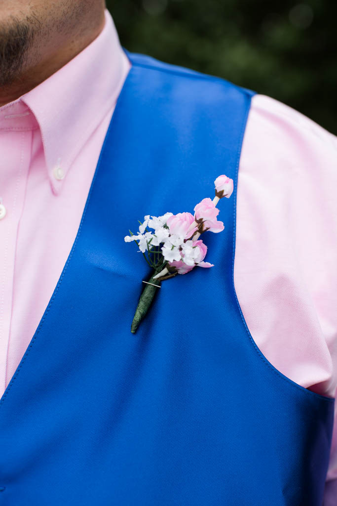 smple pink and white flower boutoneirre that is pinned on the groom's royal blue vest