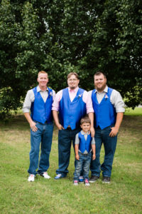 groom stands with his two groomsmen and ring bearer all dressed in royal blue vests