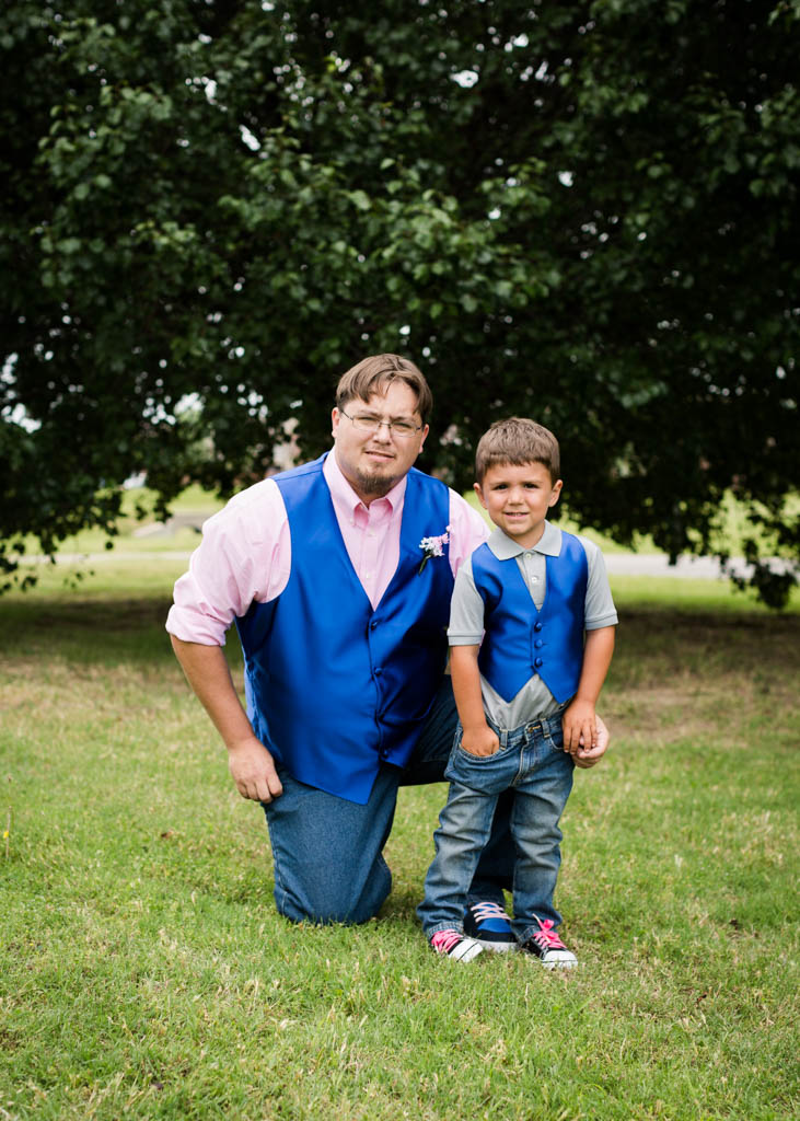 groom wering a royal blue vest and pink shirt kneels next to his ring bearer