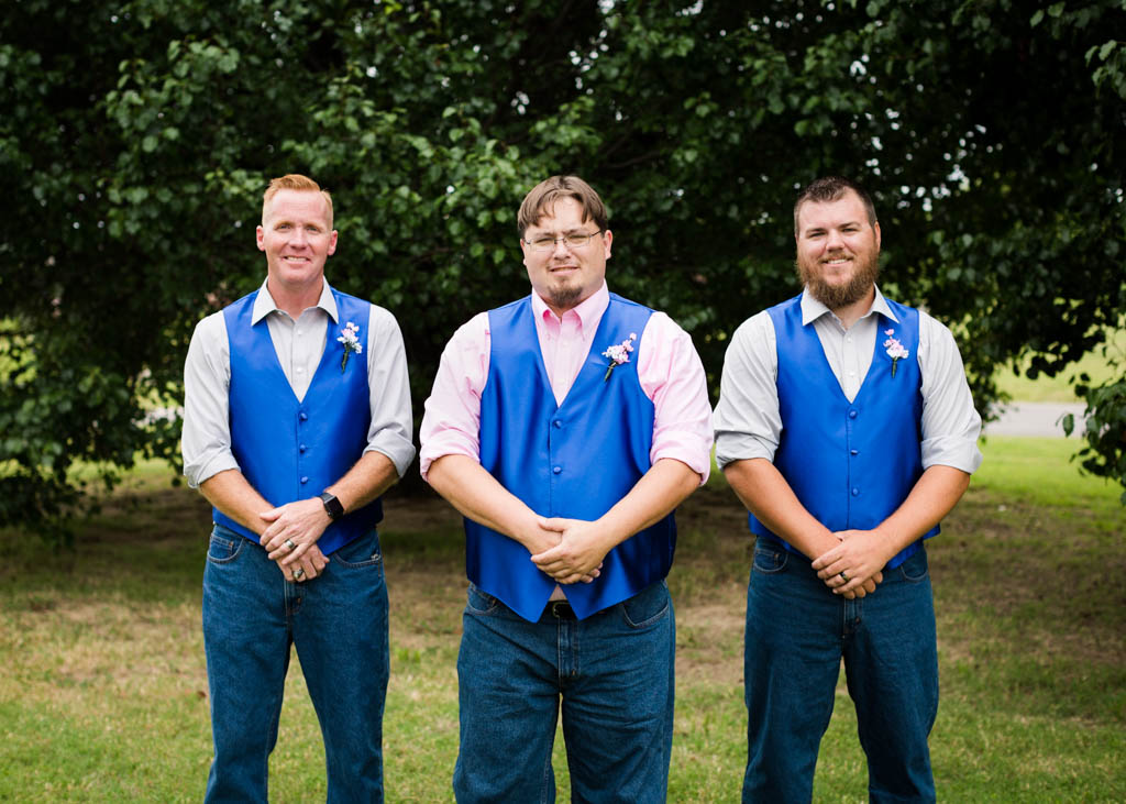 groom stands in the middle of his two groomsmen with their hands folded in front of them