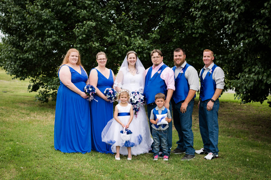bride and groom pose in the grass with their wedding party dressed in royal blue and pink