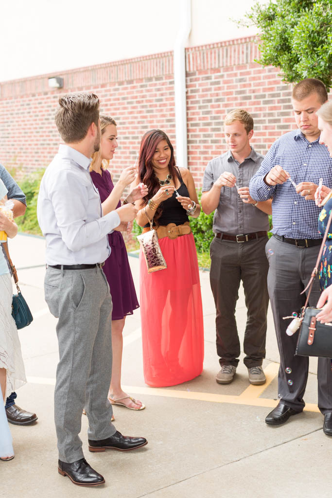 a group of young adult guests smile and laugh as they wait to blow bubbles at the bride and groom