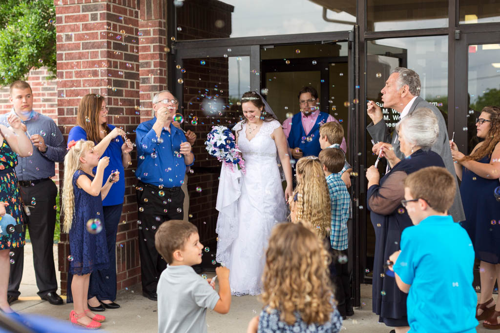 bride and groom exit the church while guests blow bubbles at them