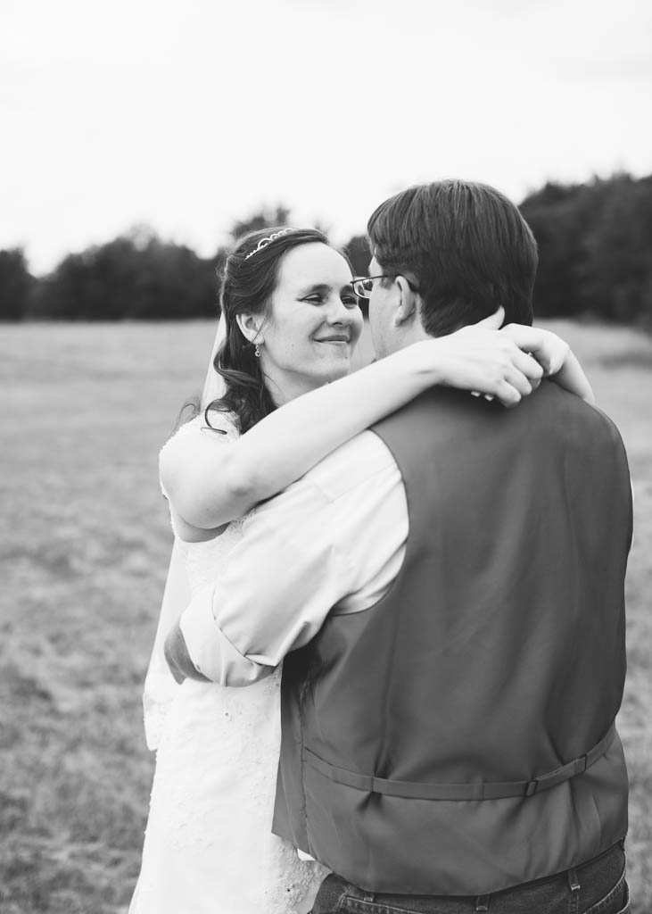 bride smile and looks in her groom's eyes while they embrace in a field