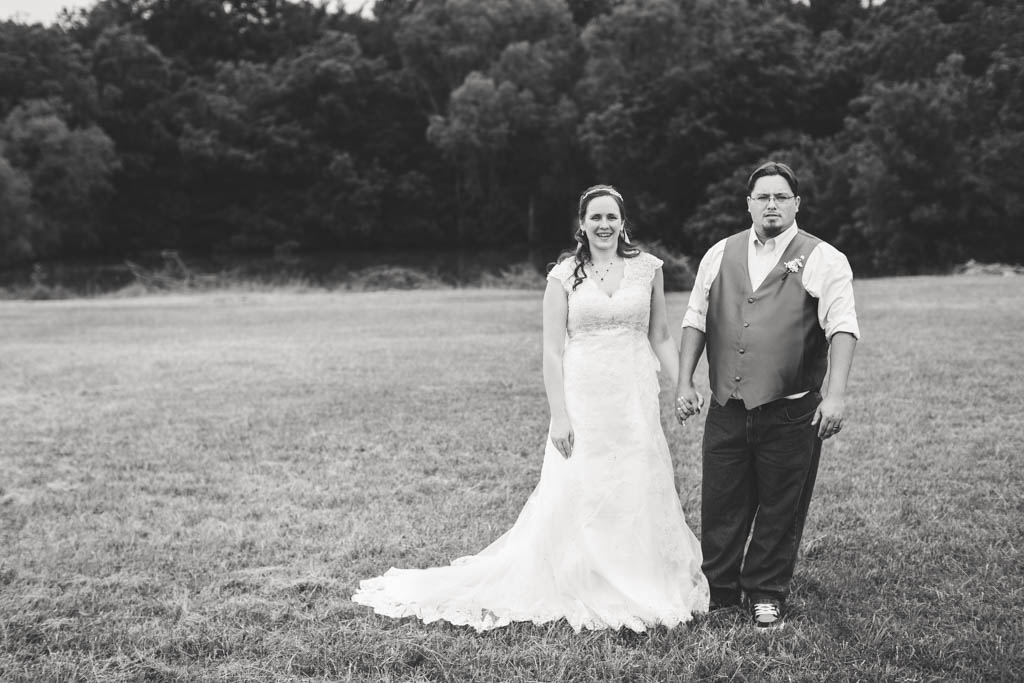 bride and groom stand side by side holding hands and smiling in a field