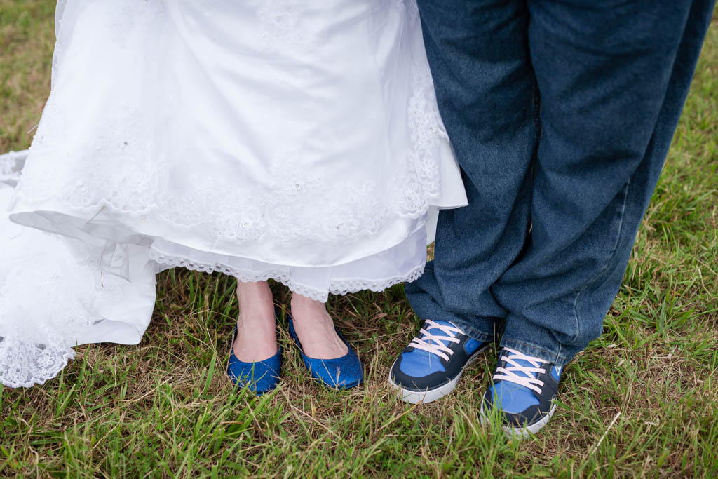 the bride lifts her dress to reveal her sparkley royal blue flats next to her husband's royal blue and pink sneakers
