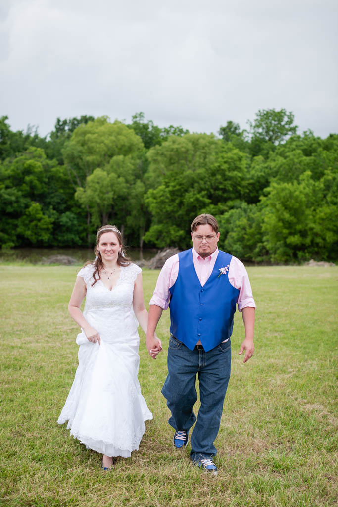 bride and groom hold hands as they walk through a field