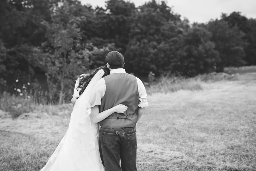 bride wraps her arm around the groom's back and rests her head on his shoulder while they look off in the distance