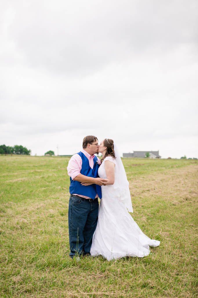 bride and groom hold each other and kiss in the middle of a field