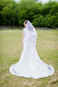 bride stands in a field and looks over her shoulder with her back turned to the camera