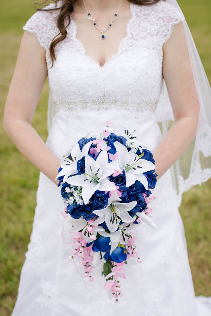 closeup of bride holding her blue and pink bouquet that is filled with white lillies