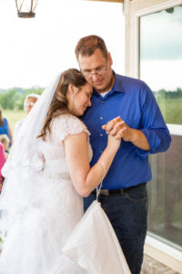 bride rests her head on her dad's chest while they dance on the front porch