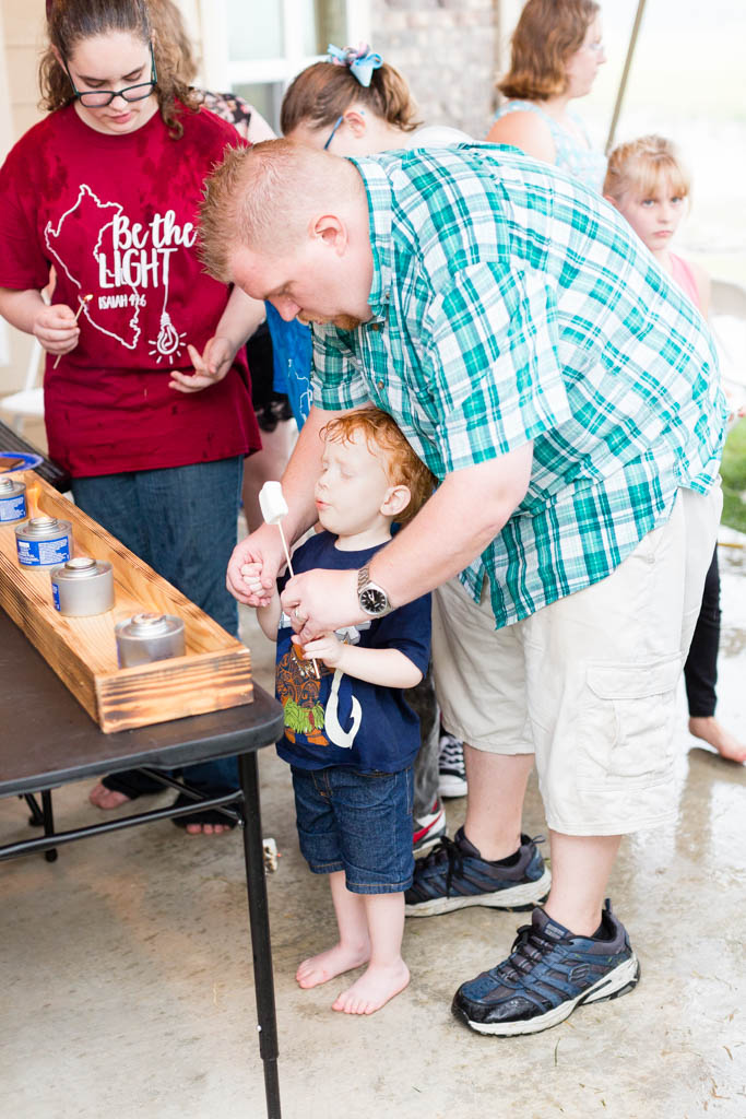 A father helps his redheaded son make a smore at the smores bar