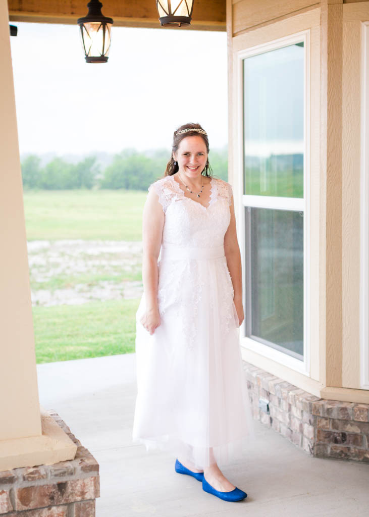 bride smiles and gently grasps her white reception dress on the front porch 