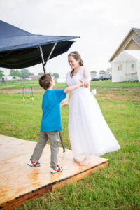 bride in a white dress and a little boy giggle and dance on a dance floor on the lawn