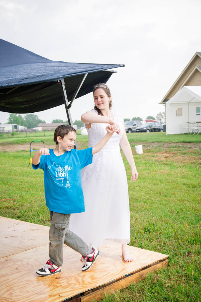 bride wearing a white reception dress spins a little boy on the dance floor on the lawn