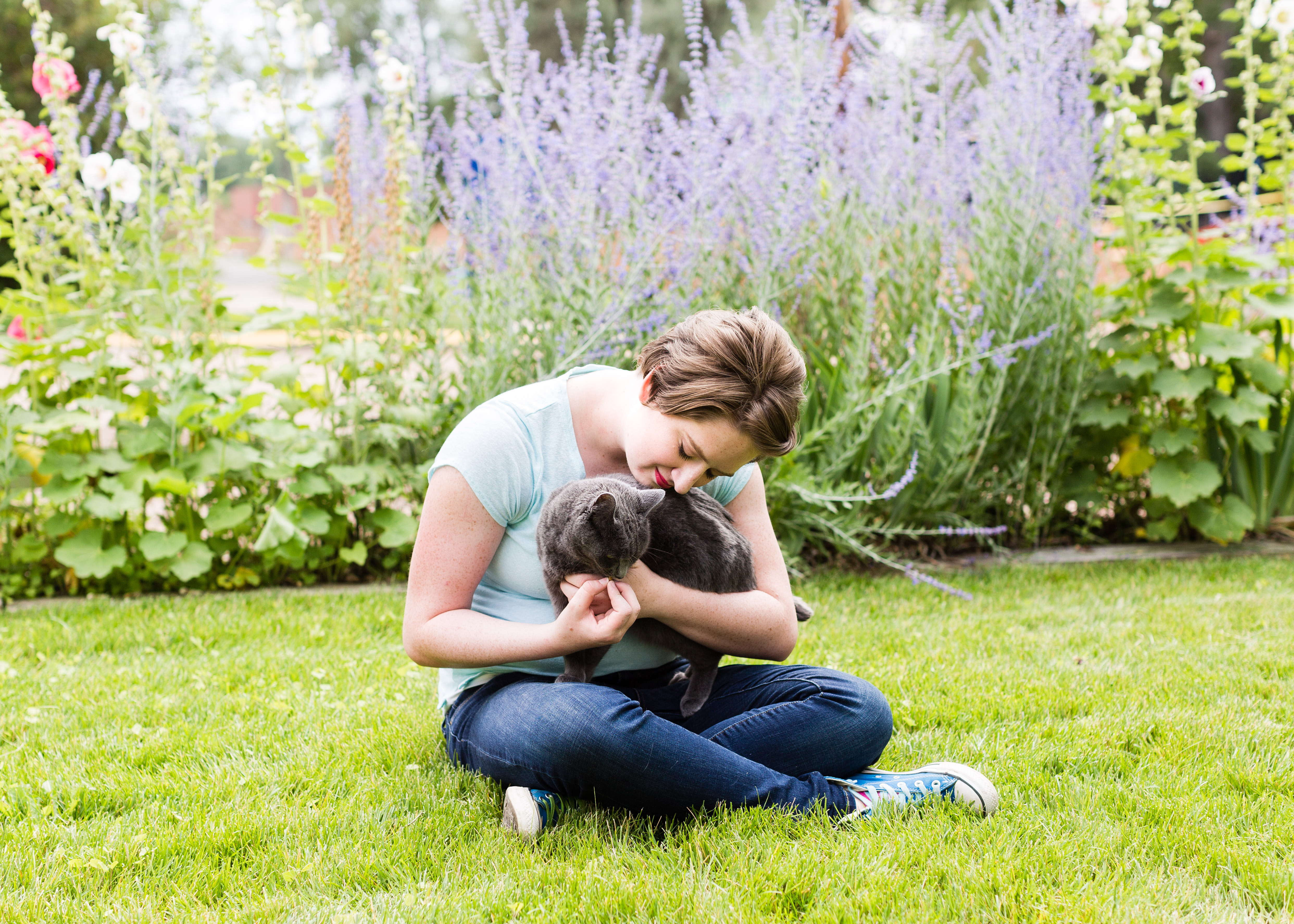 Senior girl snuggling dark grey cat on her lap in the grass