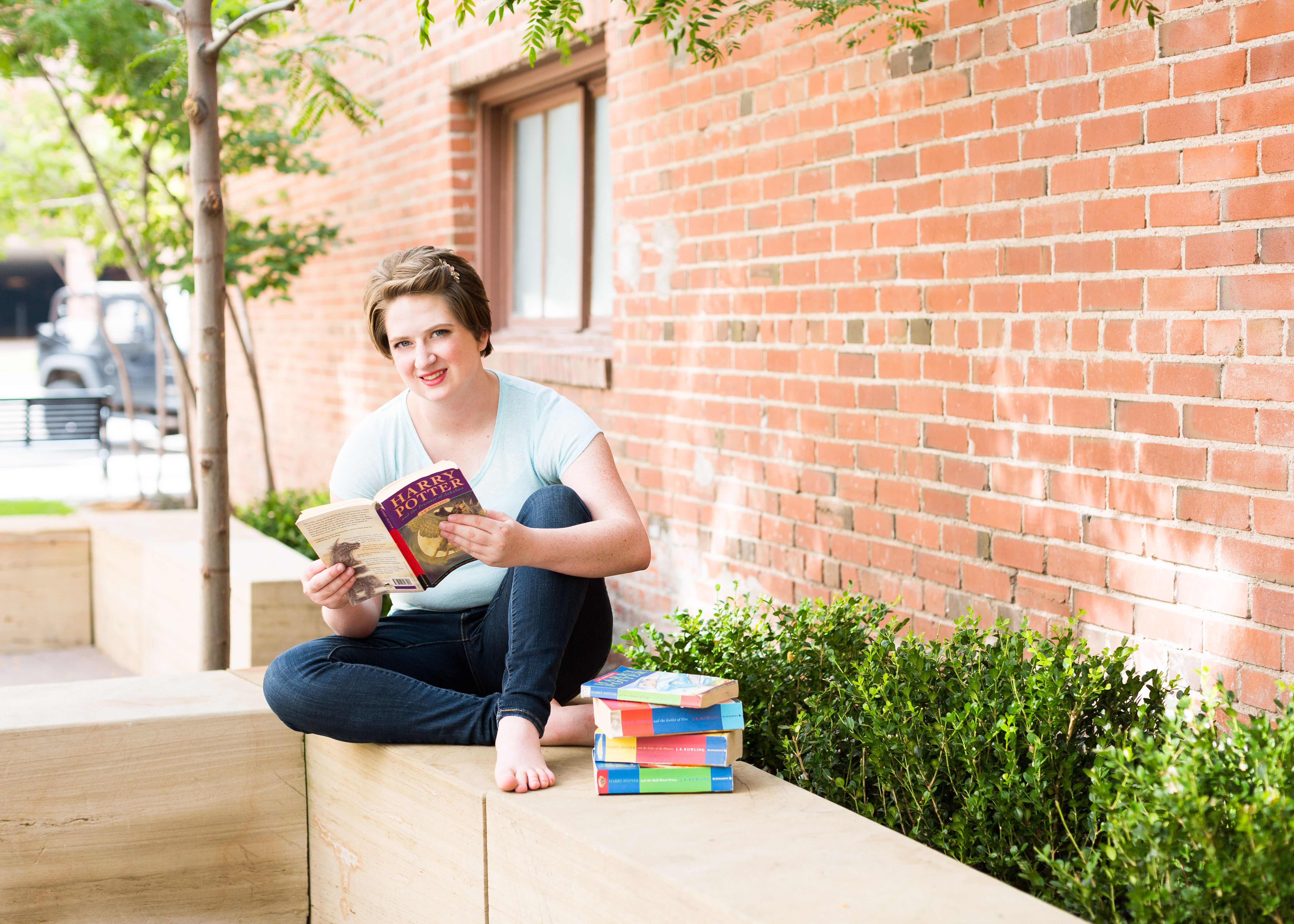 Senior girl sits with her legs crossed on a bench while reading Harry Potter books