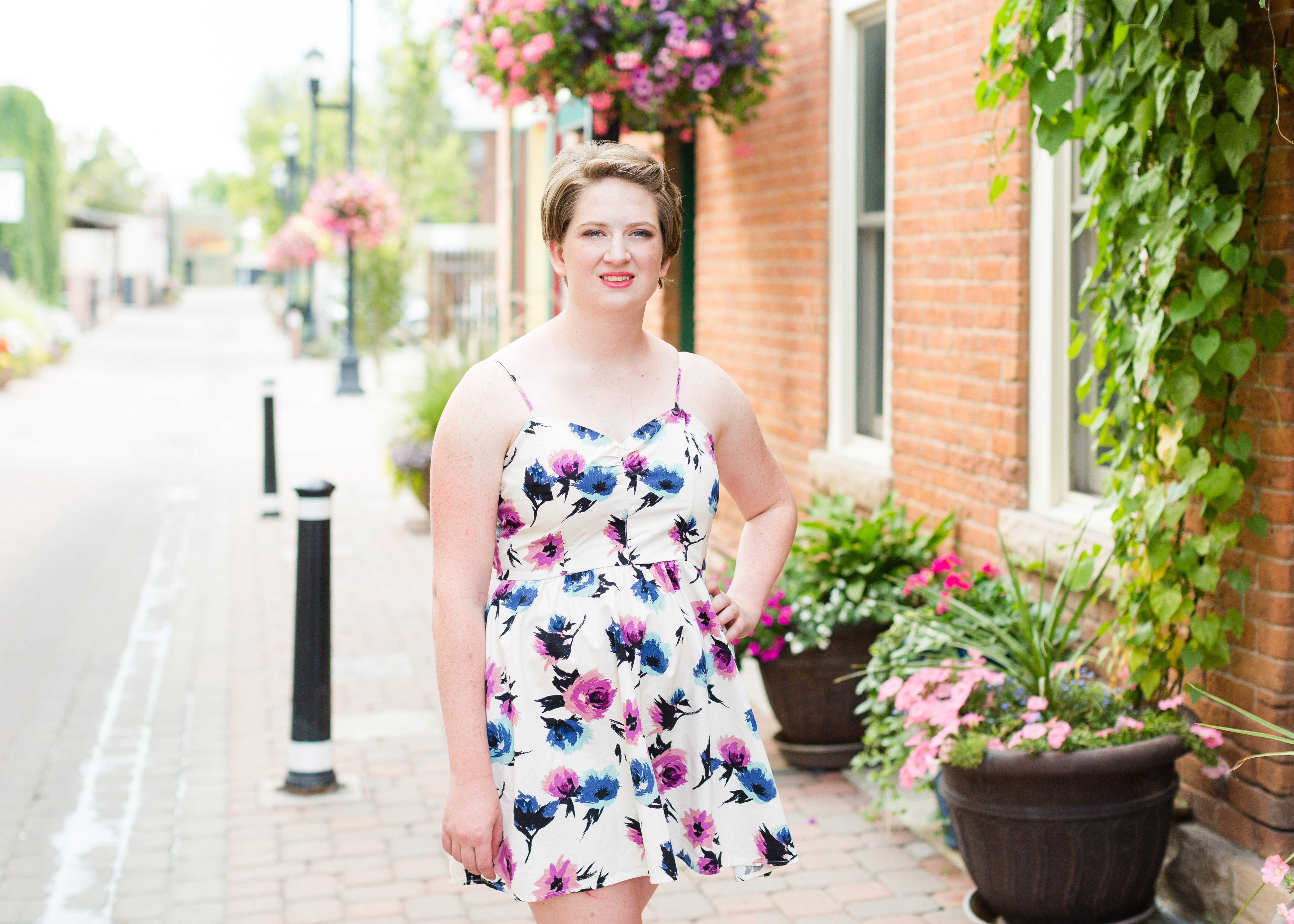 senior girl wearing white floral dress stands with her hand on her hip in an alley filled with flowers