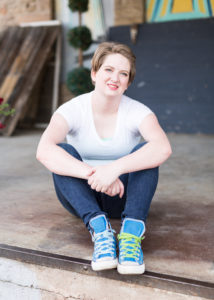 Senior girl wearing a white t-shirt, jeans and blue high top converse sneakers sits with her elbows resting on her knees and smiles