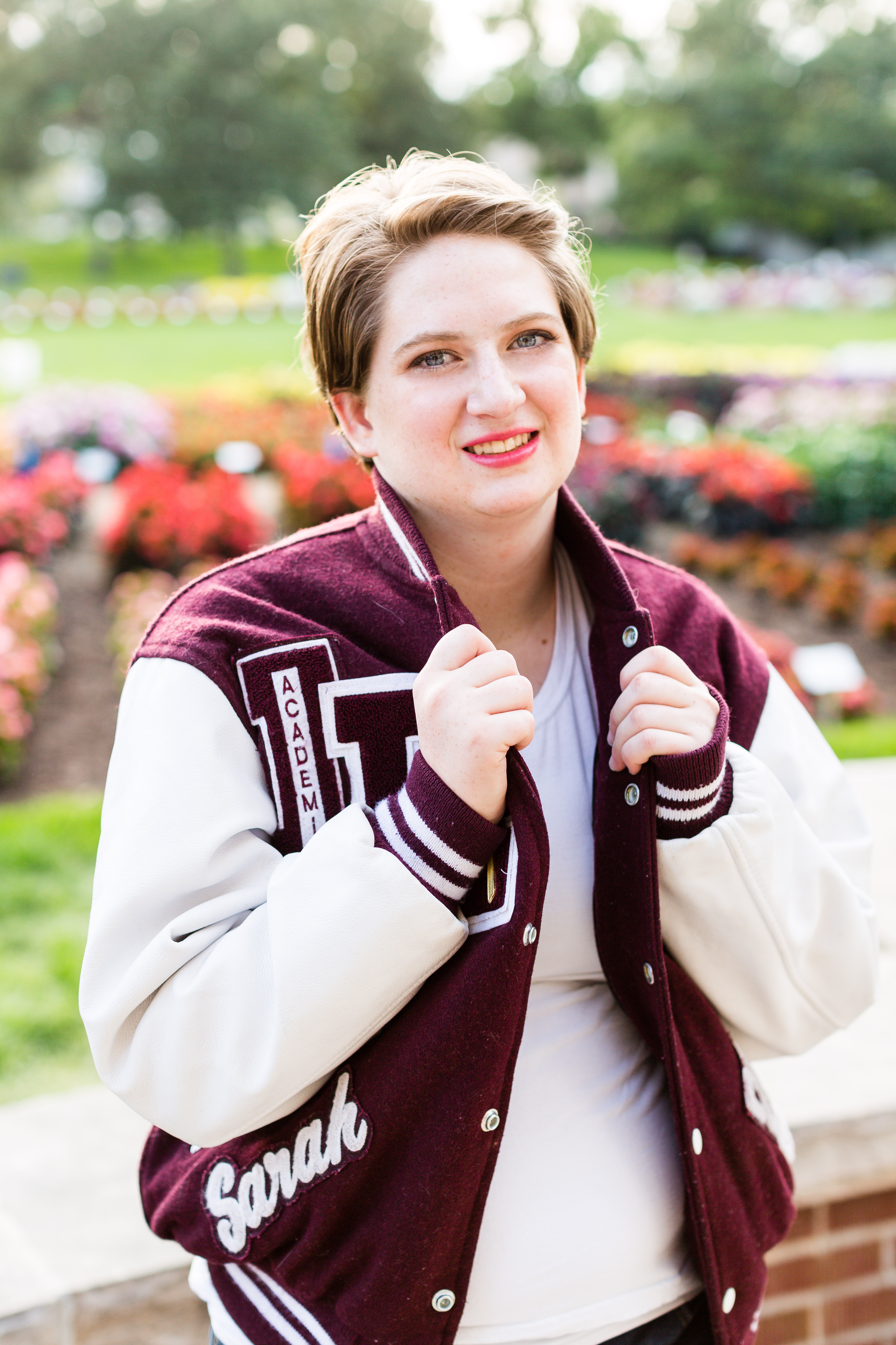 senior girl smiles and holds the collar of her maroon and white Letterman Jacket