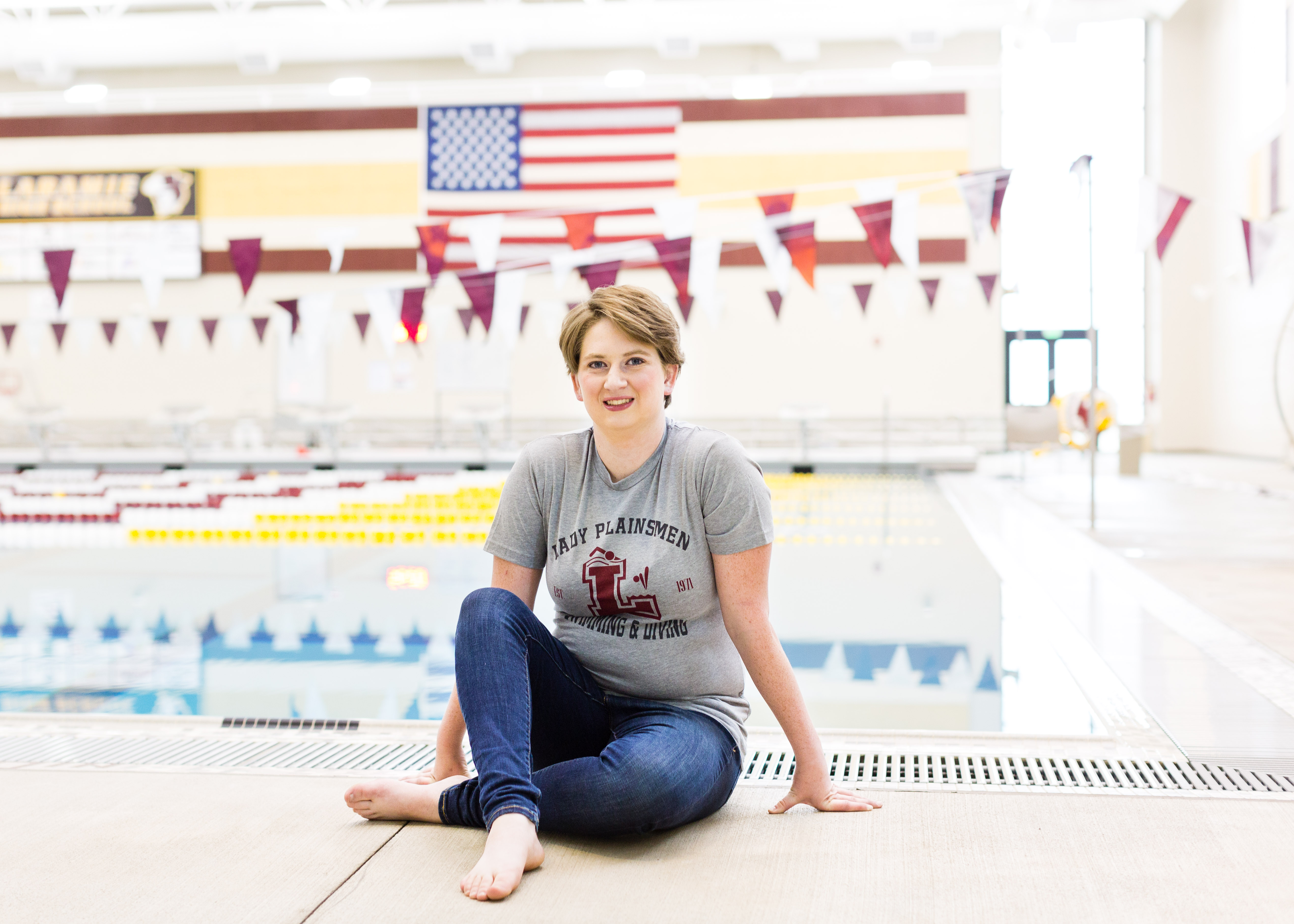 senior girl wearing grey Laramie Plainsmen t Shirt and jeans sits on the of a pool