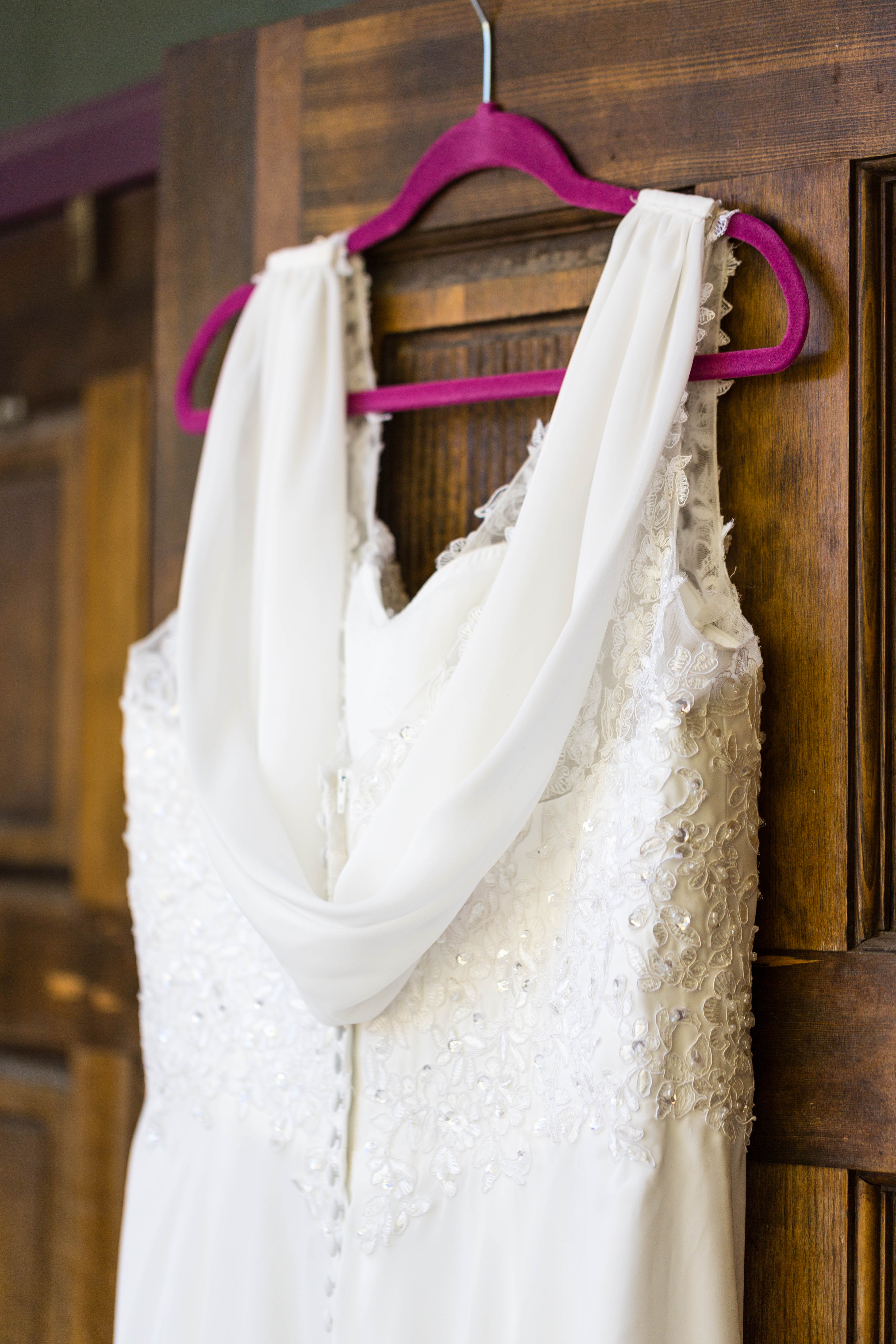 back of lace and beaded wedding dress hanging from wooden door