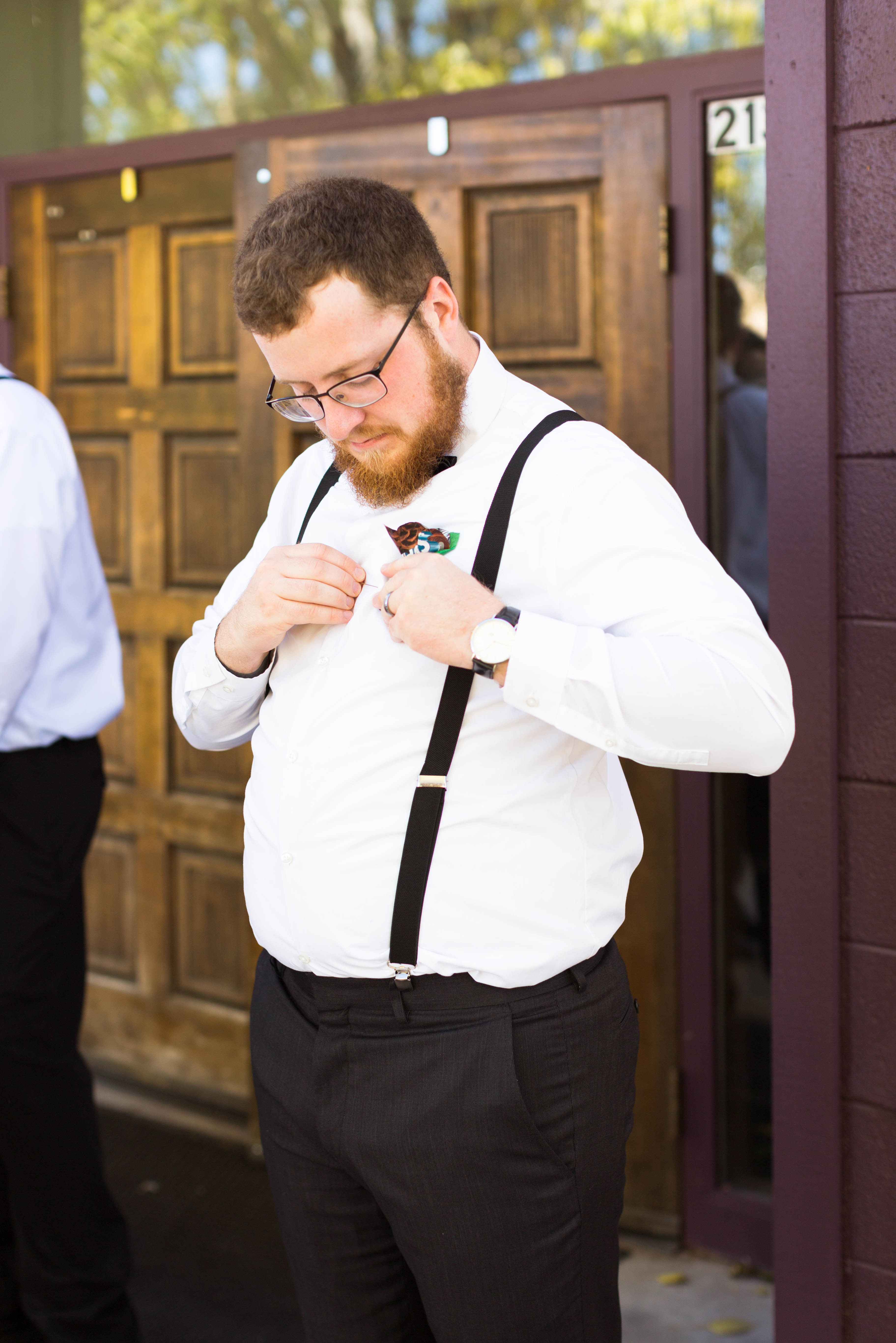 best man puts on his boutonniere outside of the church