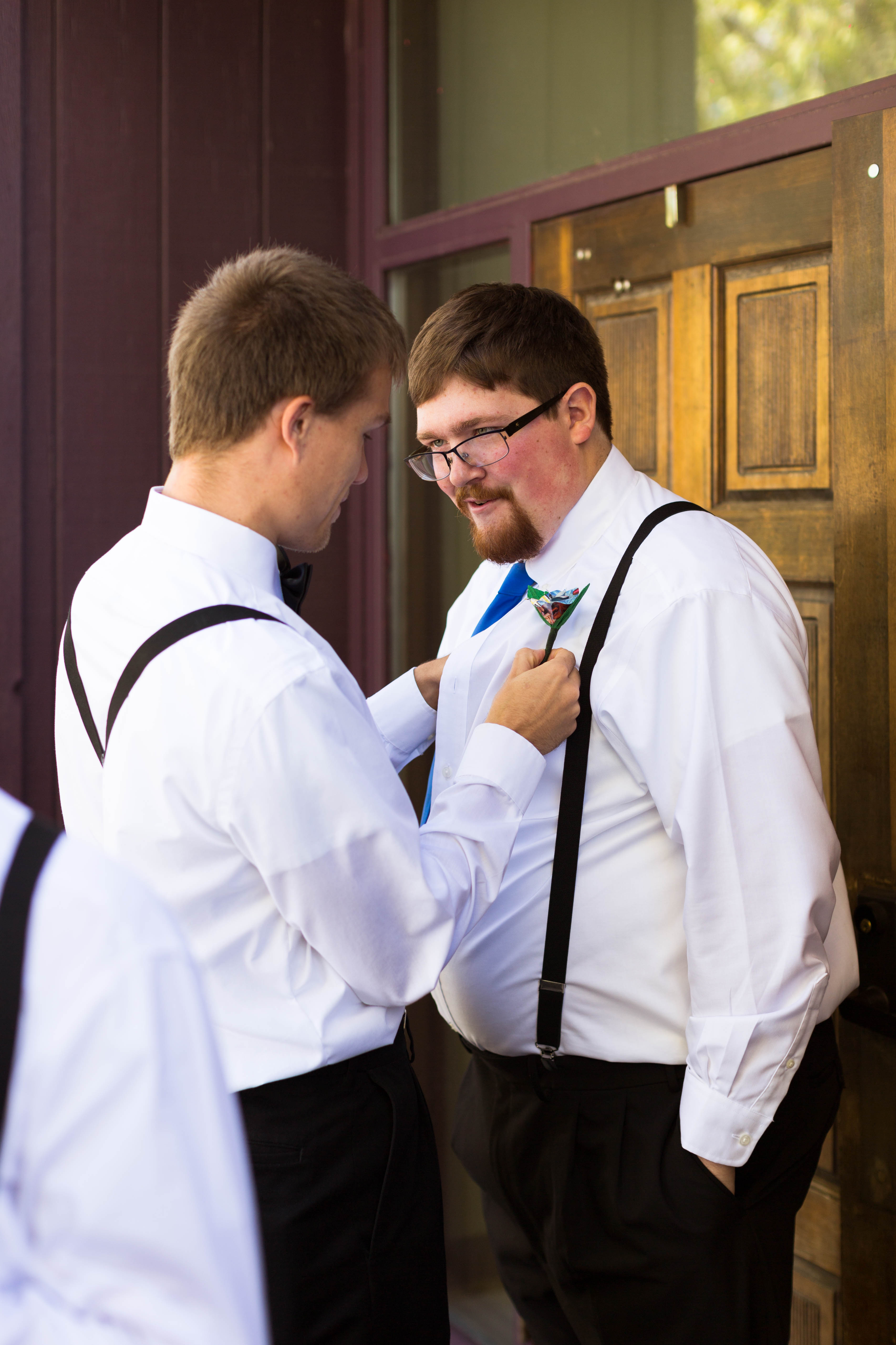 groom smiles as his best man helps him put on his boutonniere