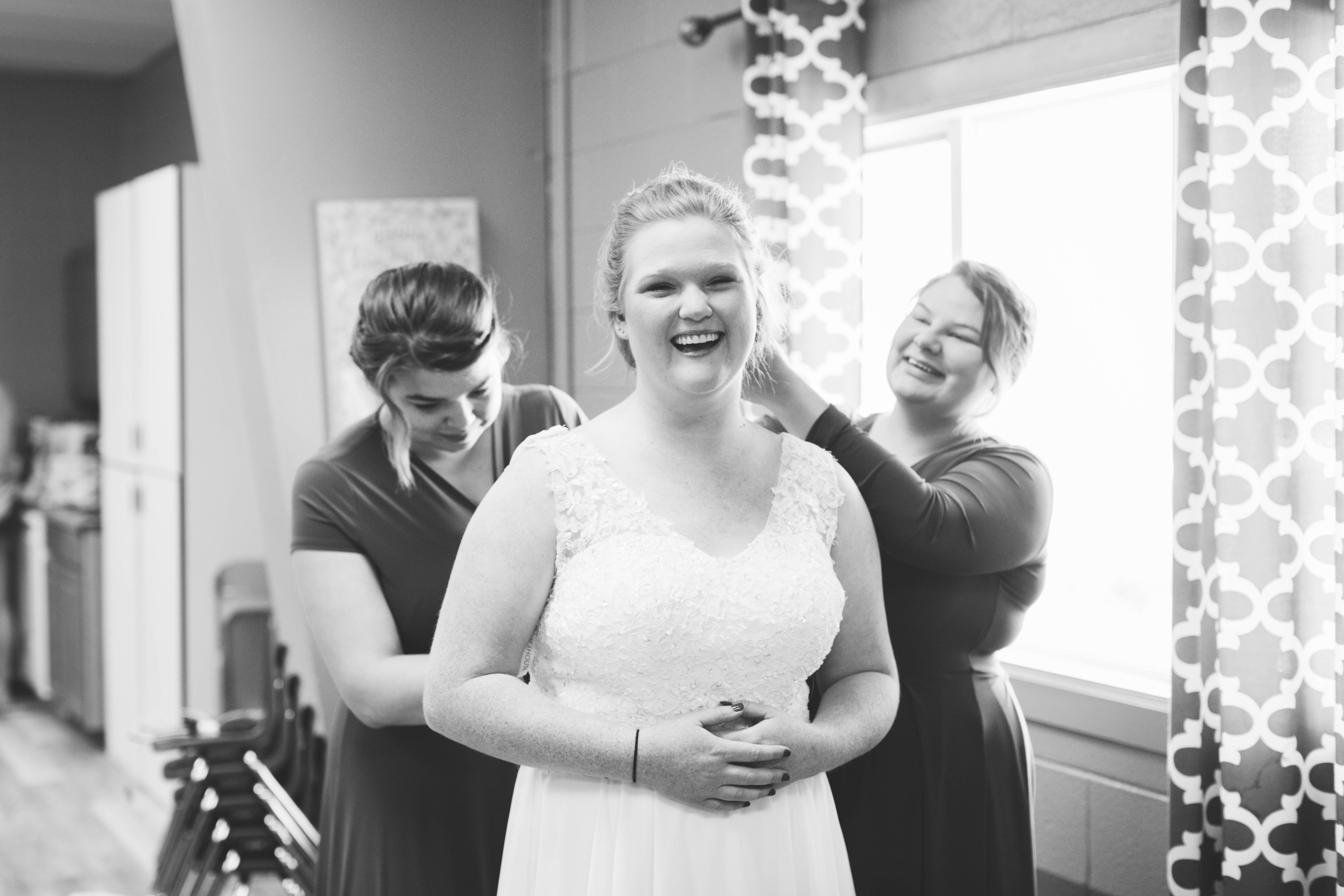 bride smiles as maids of honor help her into her dress