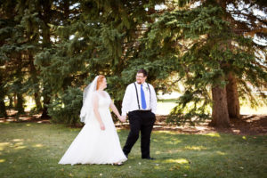 bride and groom hold hands and walk through the park