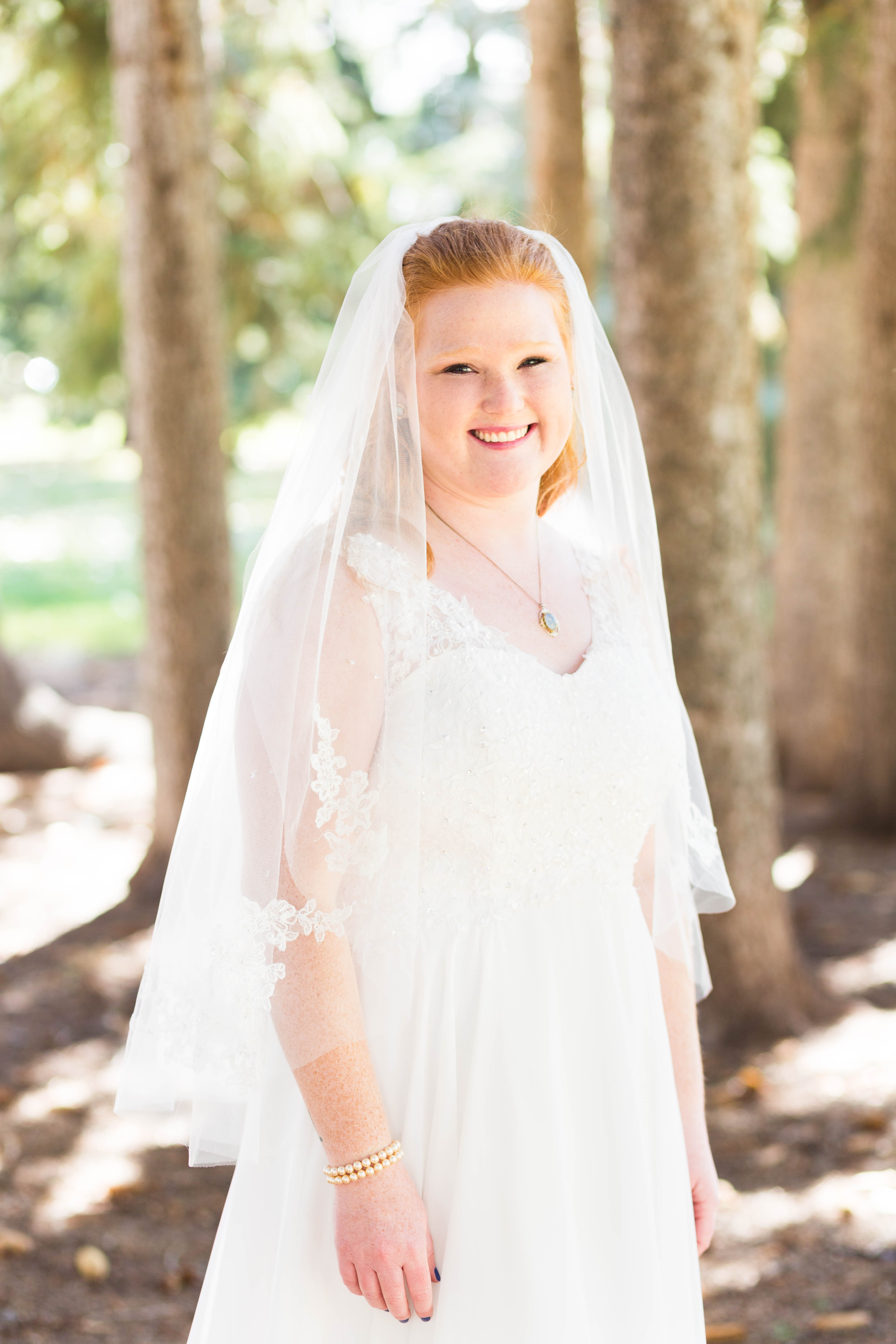 bride smiles as she stands in a stand of pine trees
