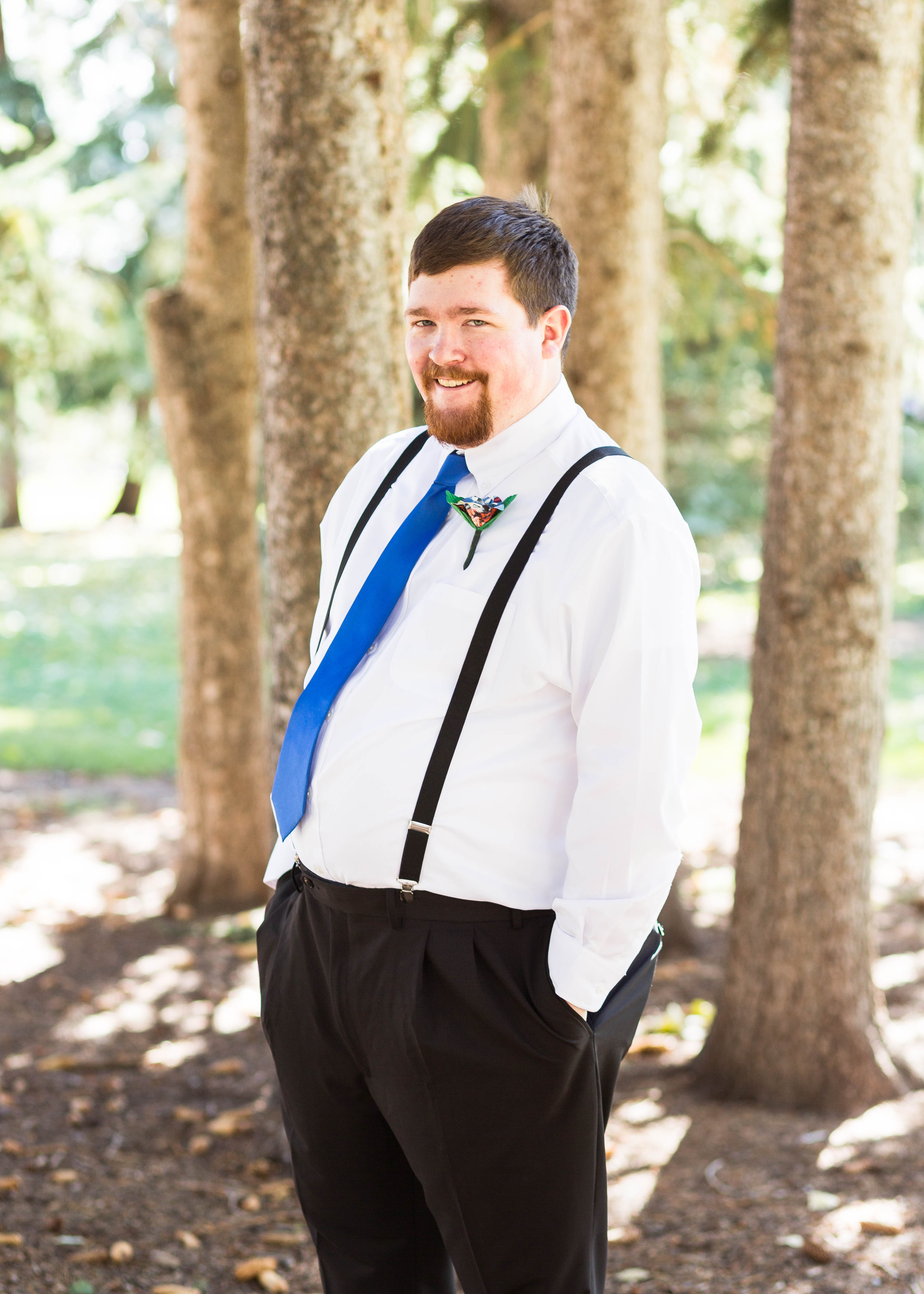 groom smiles as he stands amongst pine trees
