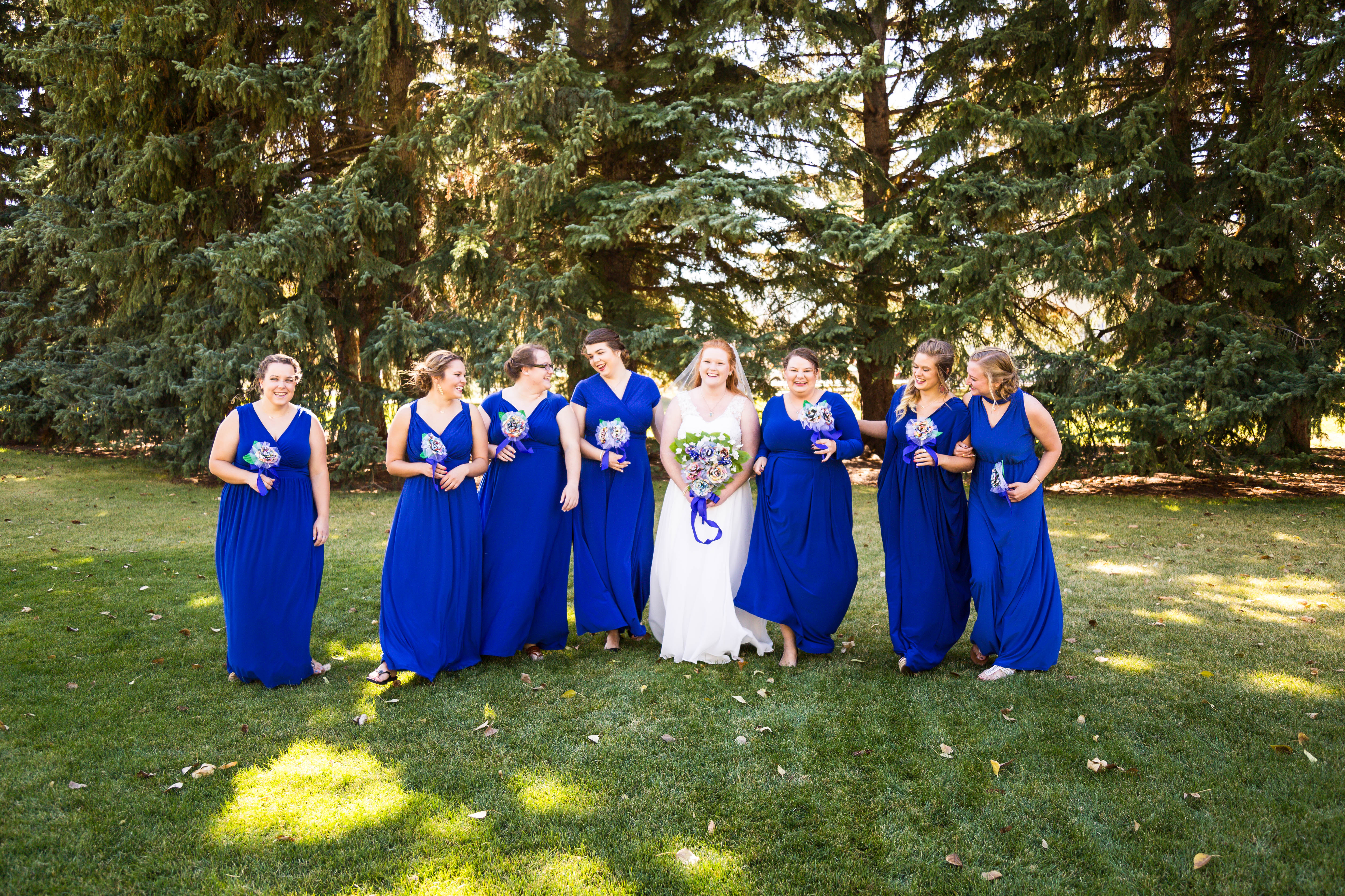 bride laughs and smiles as she walks through park with bridesmaids
