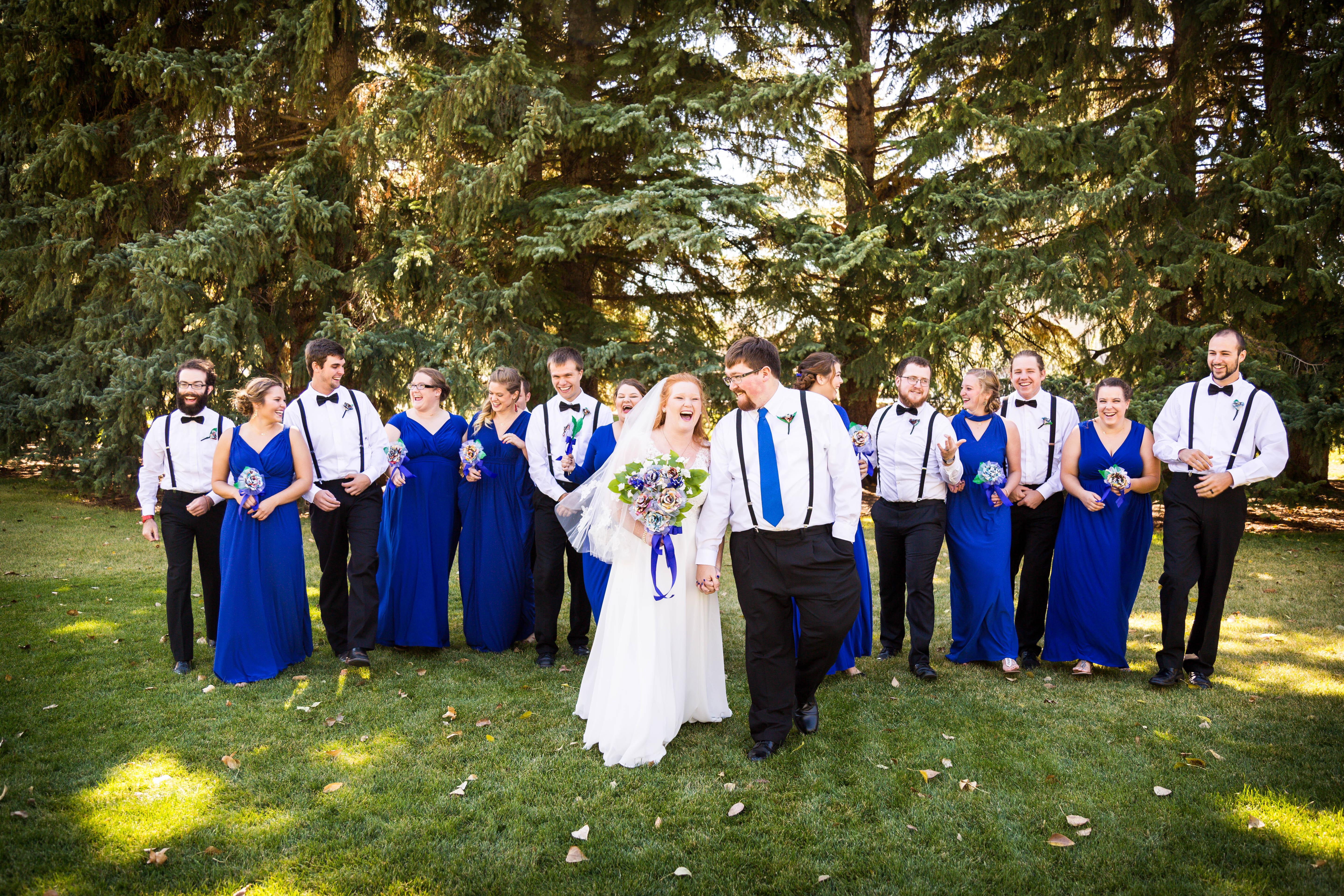 bride and groom hold hands and laugh as they walk with wedding party