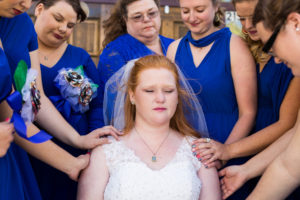 bride tears up as bridesmaids pray over her