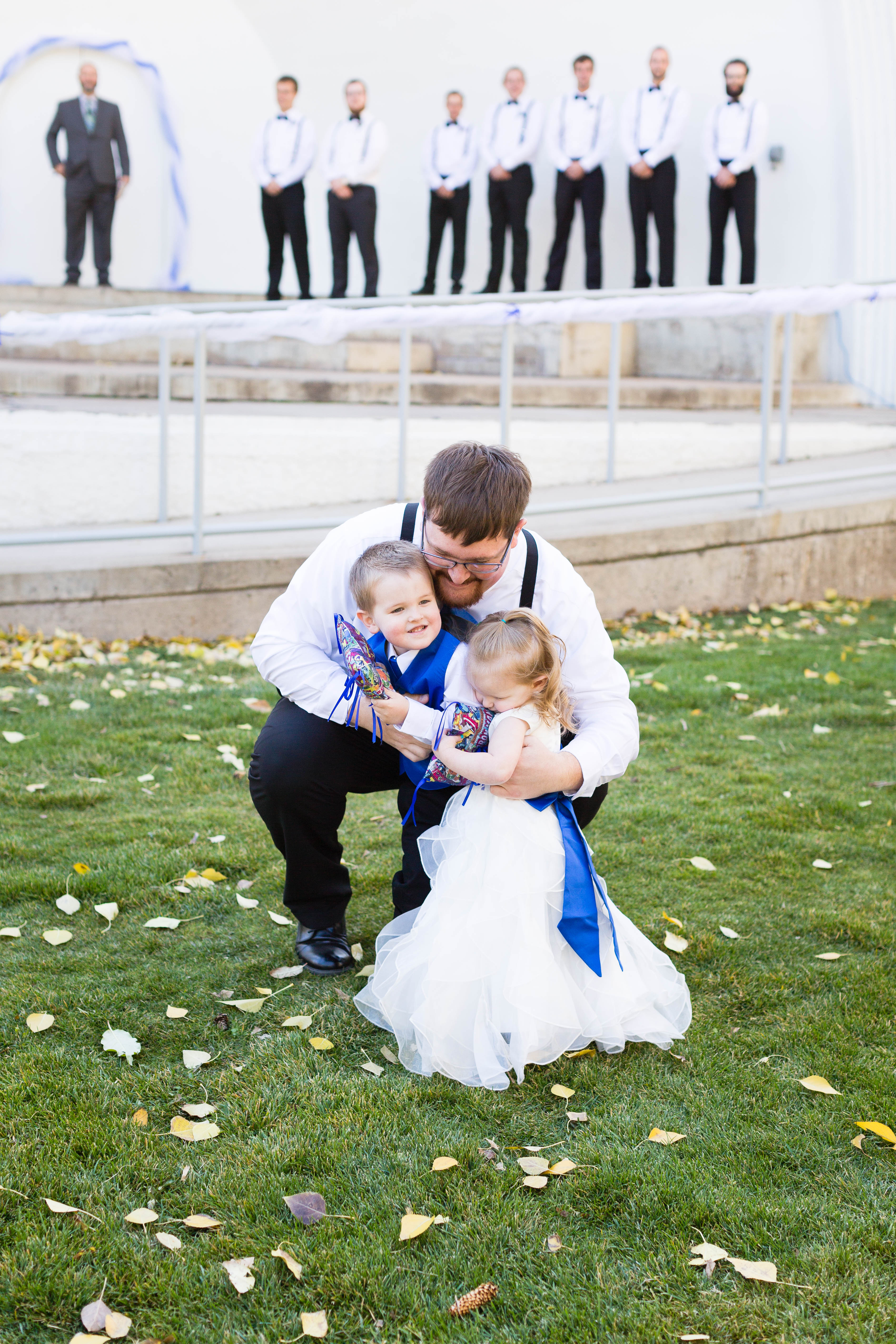 groom kneels down and hugs ring bearer and flower girl after they walk down the aisle