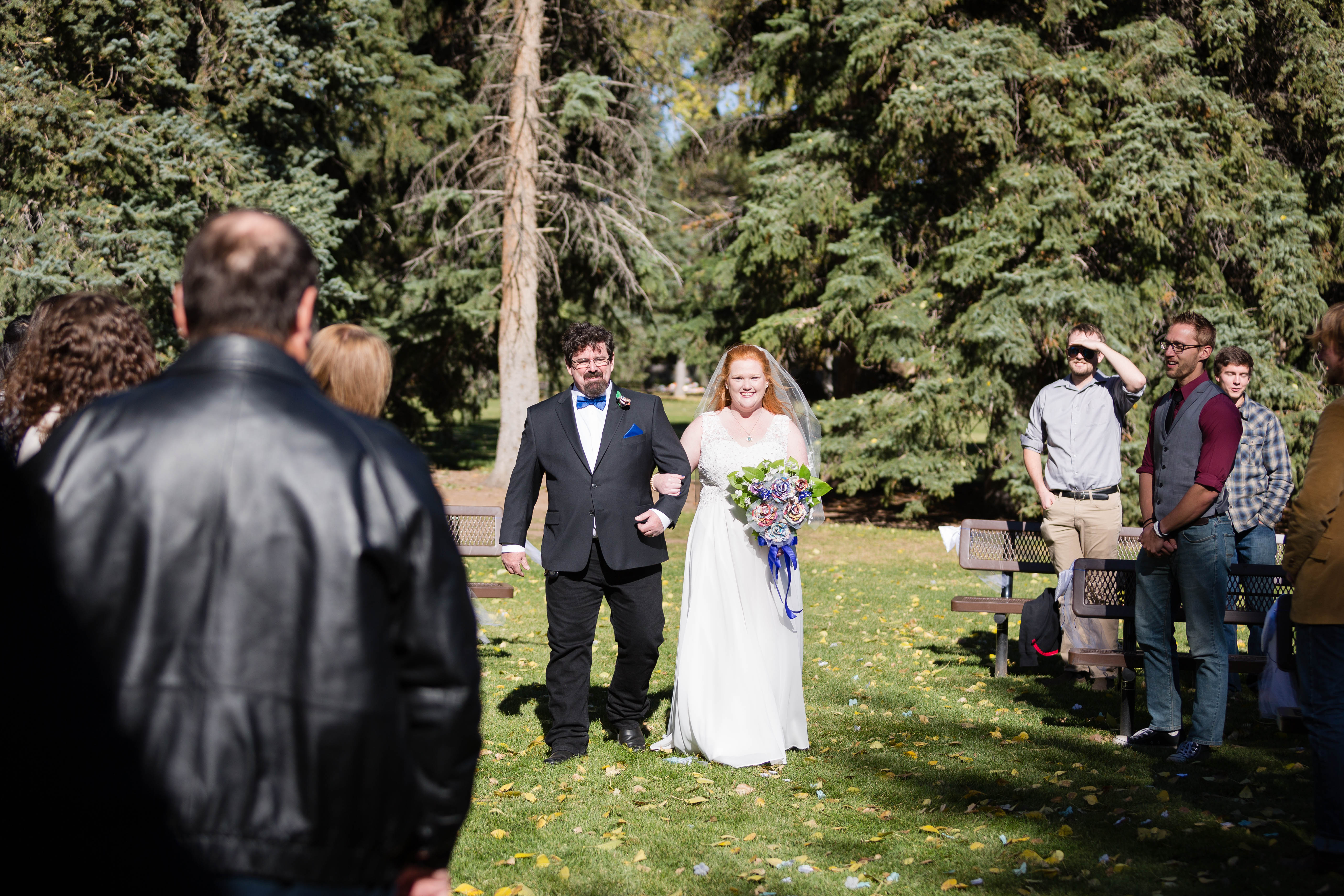 bride smiles as father walks her down the aisle in the park