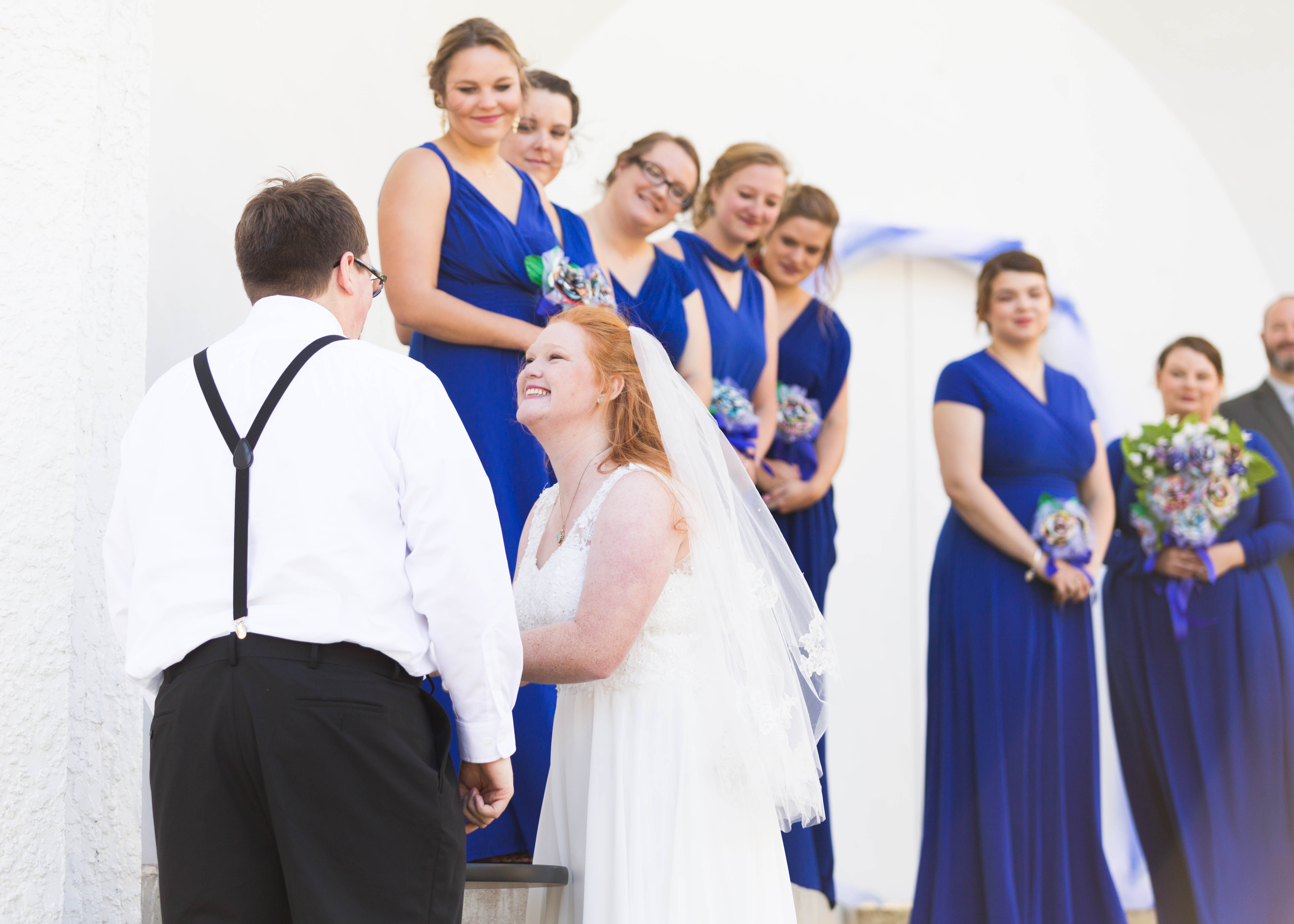 bridesmaids watch as bride smiles as she shares communion with groom n