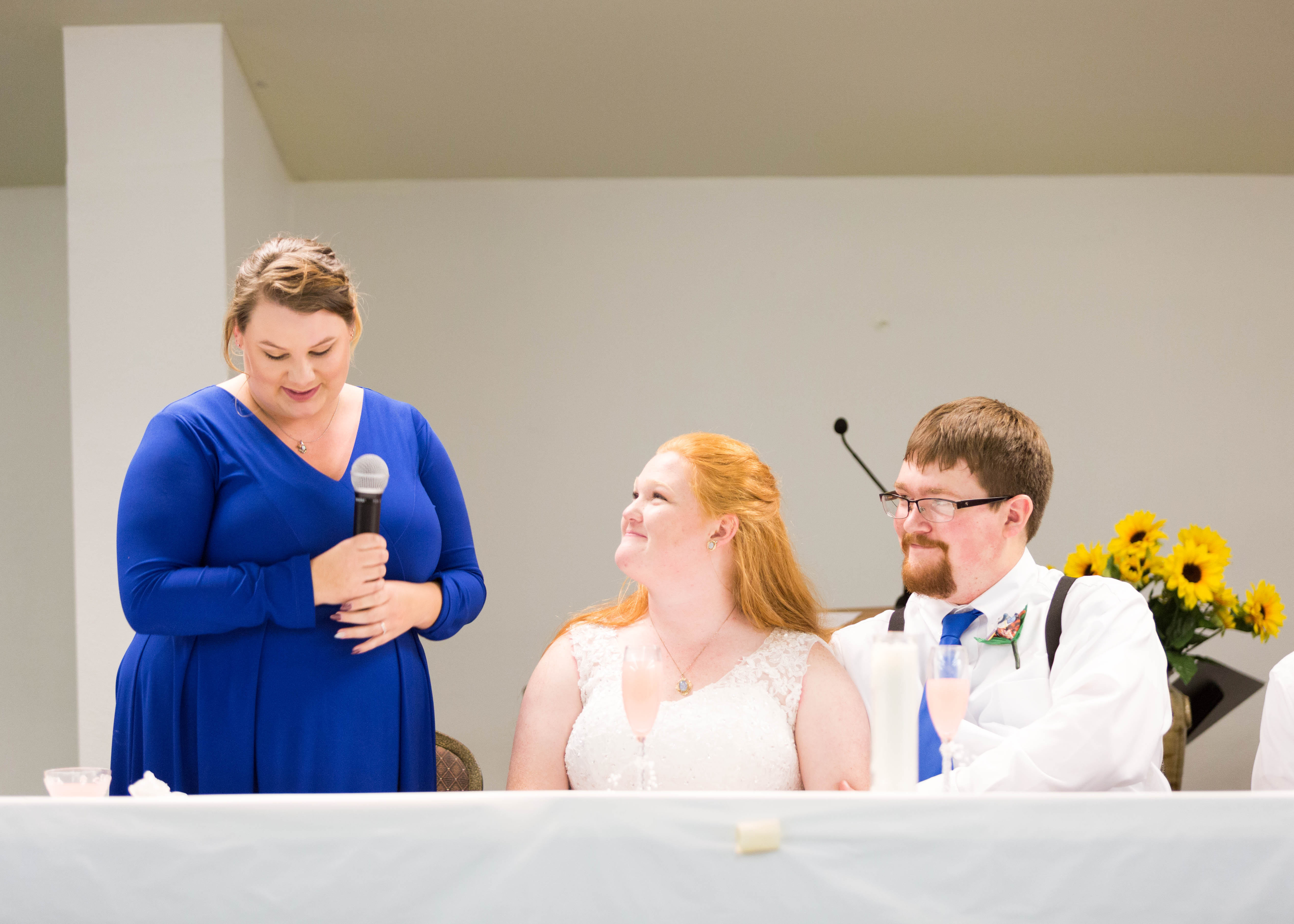 bride and groom smile while bridesmaid gives her speech