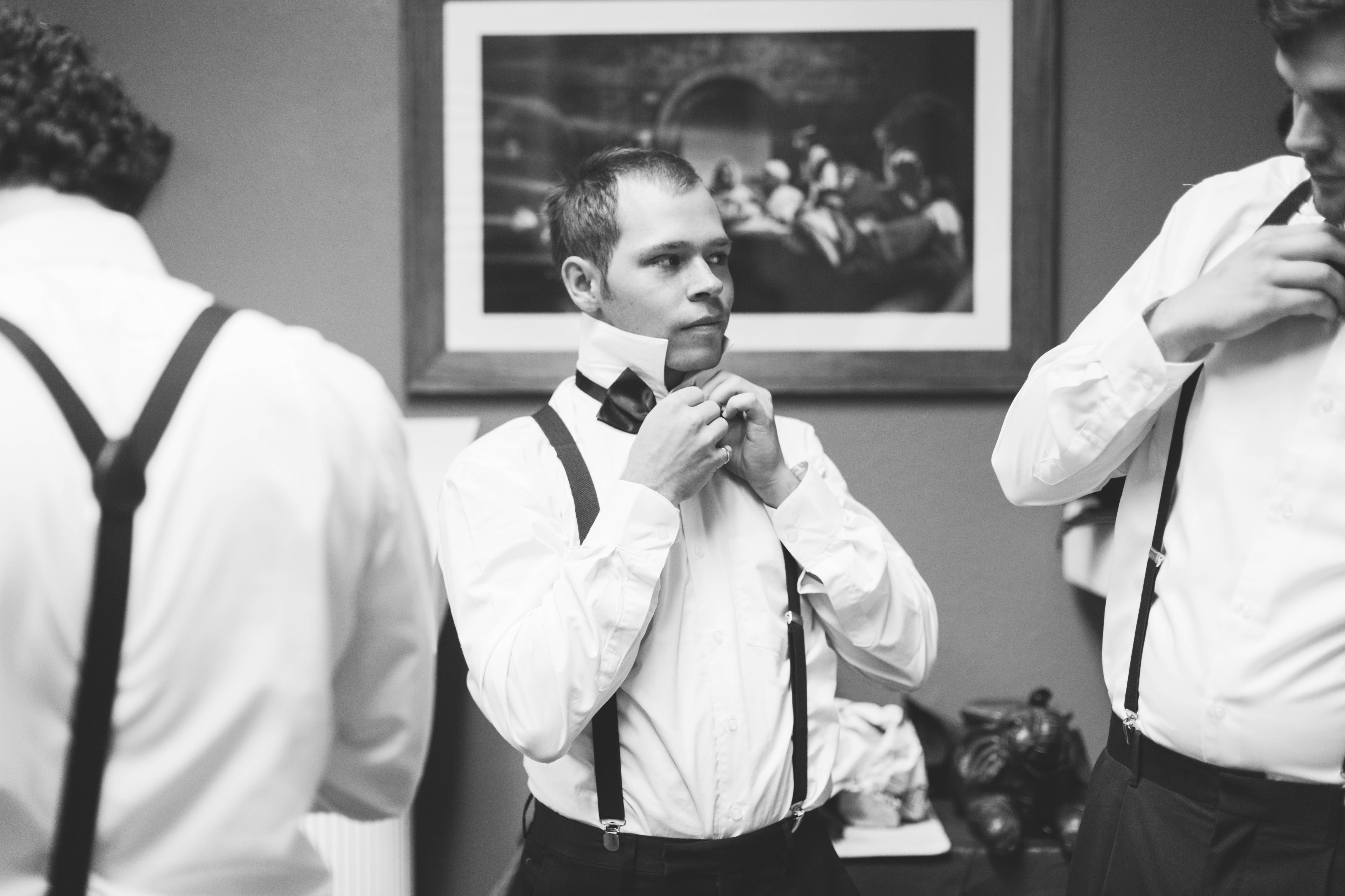 groomsman lifts his collar and adjusts his bow tie